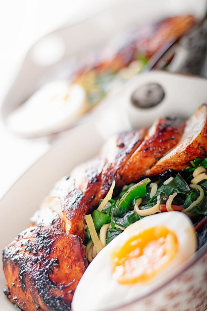 Portrait extreme close up image of a hoisin chicken breast with an out of focus jammy boiled egg