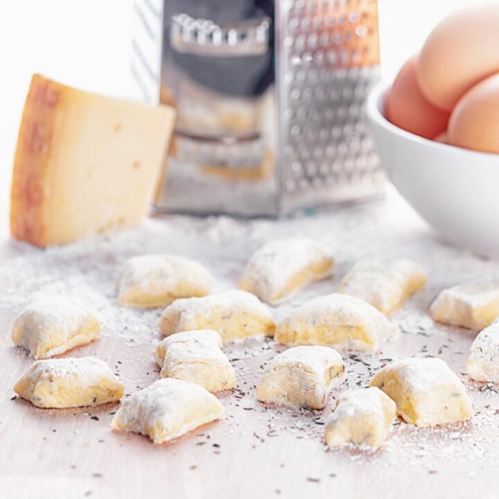 Square image of homemade potato gnocchi served on a board with a grater, eggs and parmesan cheese