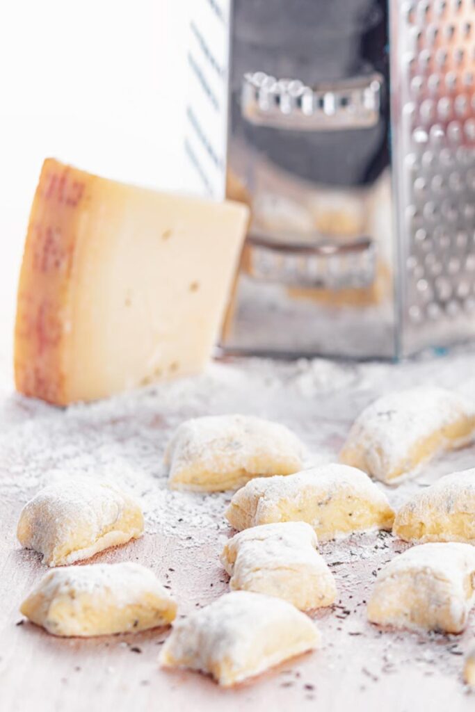 Portrait image of homemade potato gnocchi served on a board with a grater, eggs and Parmesan cheese