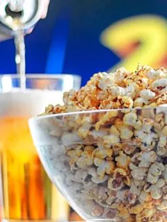 Portrait image of spiced popcorn in a glass bowl with a beer being poured in the background