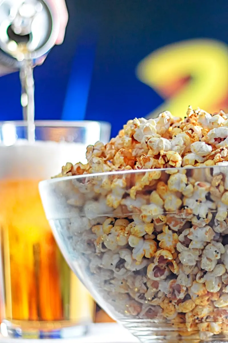 Portrait image of spiced popcorn in a glass bowl with a beer being poured in the background