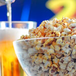 Portrait image of spiced popcorn in a glass bowl with a beer being poured in the background with text overlay