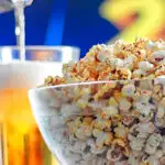 Portrait image of spiced popcorn in a glass bowl with a beer being poured in the background with text overlay