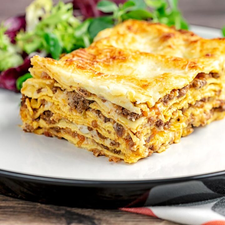 Square image of a classic Lasagna bolognese served as a slice on a plate showing layers