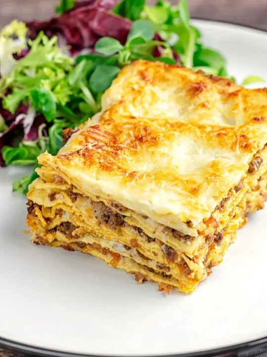 Portrait image of a classic Lasagna Bolognese served as a slice on a plate with side salad