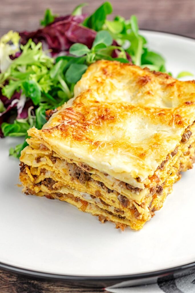 Portrait image of a classic Lasagna Bolognese served as a slice on a plate with side salad