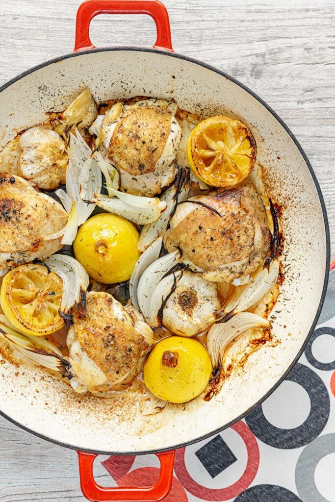 Portrait overhead image of chicken thighs cooked with onion lemon and garlic in an enamel cast iron pot