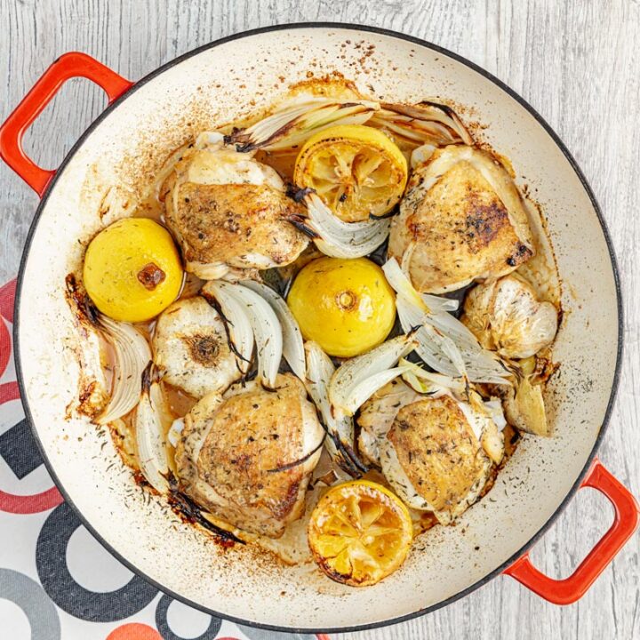 Square overhead image of chicken thighs cooked with onion lemon and garlic in an enamel cast iron pot