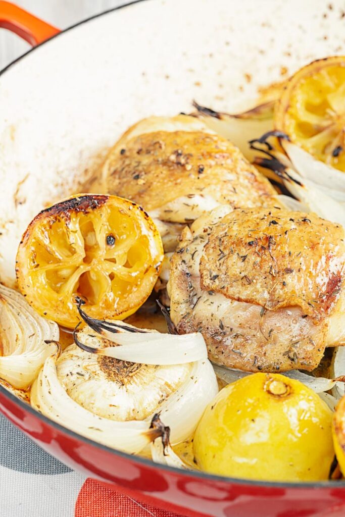 Portrait close up image of chicken thighs cooked with onion lemon and garlic in an enamel cast iron pot