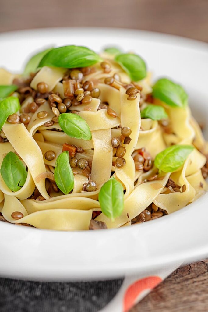 Portrait image of a vegetarian lentil bolognese served in a while bowl garnished with basil leaves