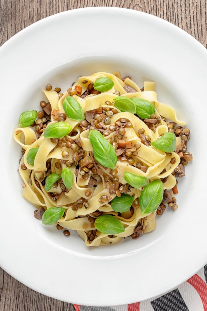 Portrait overhead image of a vegetarian lentil bolognese served in a while bowl garnished with basil leaves