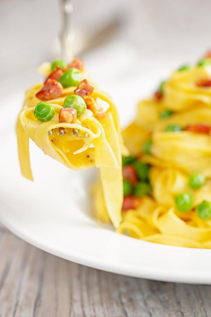 Portrait close up image of pasta carbonara with peas with a mouthful on a fork and the dish out of focus