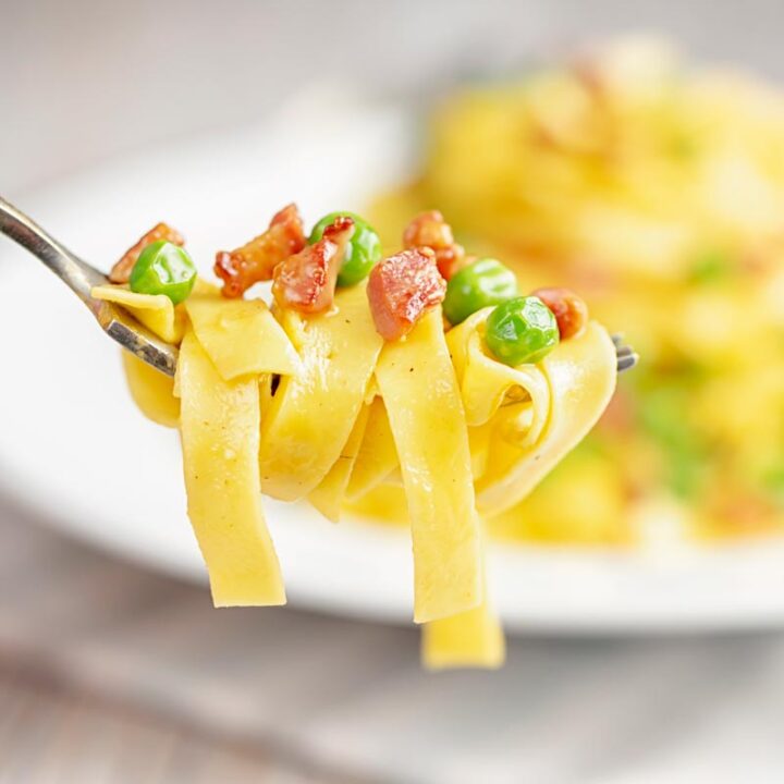 Square close up image of pasta carbonara with peas with a mouthful on a fork and the dish out of focus