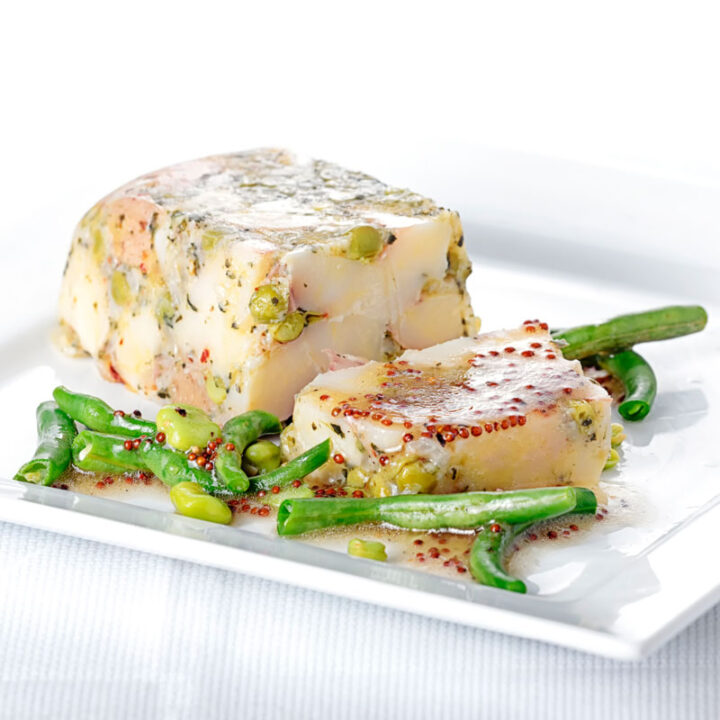 Square image of a vegetable terrine featuring peas and potatoes served on a white plate with beans and a mustard dressing