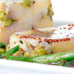 Portrait close up image of a vegetable terrine featuring peas and potatoes served on a white plate with beans and a mustard dressing