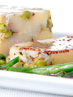 Portrait close up image of a vegetable terrine featuring peas and potatoes served on a white plate with beans and a mustard dressing