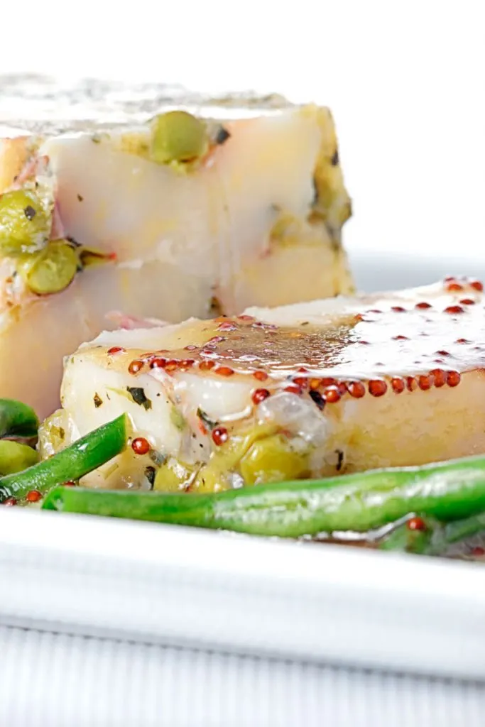 Portrait close up image of a vegetable terrine featuring peas and potatoes served on a white plate with beans and a mustard dressing