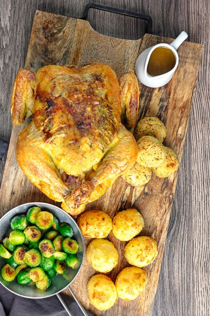 Portrait overhead image of a perfectly roast whole chicken, roast potatoes, seared Brussels sprouts, sage and onion stuffing balls and a jug of pan gravy