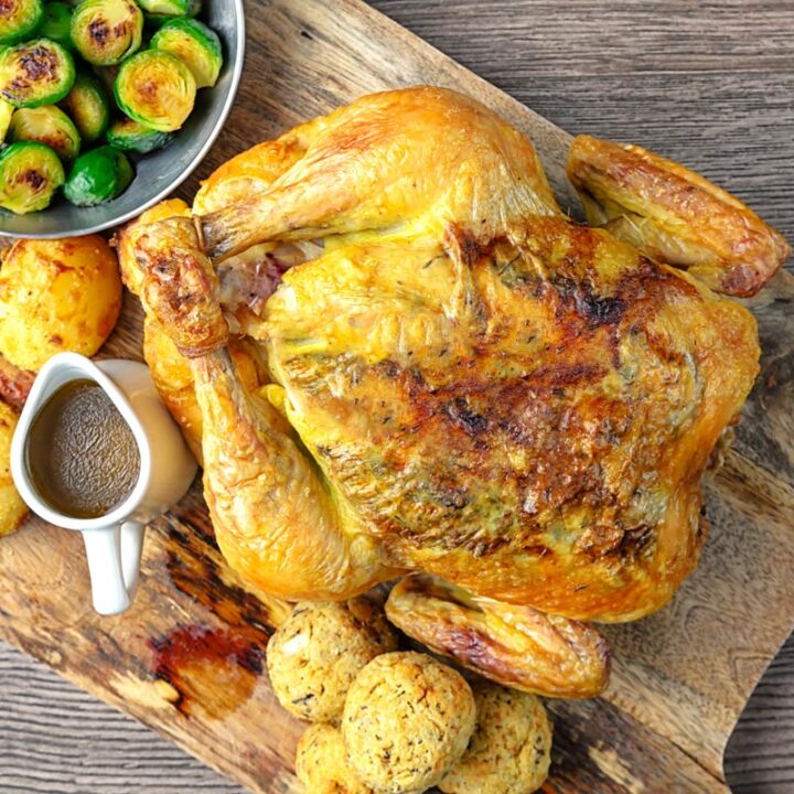 Square overhead image of a perfectly roast whole chicken, roast potatoes, seared Brussels sprouts, sage and onion stuffing balls and a jug of pan gravy