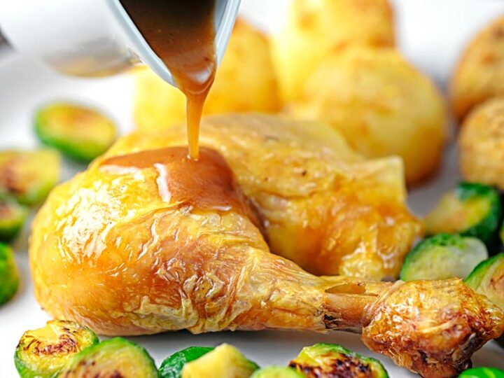 A perfect silky pan gravy being poured of over a roast chicken leg served with Brussels sprouts and roast potatoes