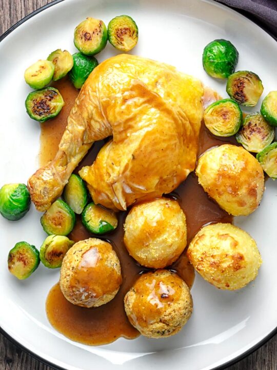 Portrait overhead image of the perfect roast chicken Sunday Lunch featuring a chicken leg, sage and onion stuffing balls, roast potatoes, sprouts and a pan gravy