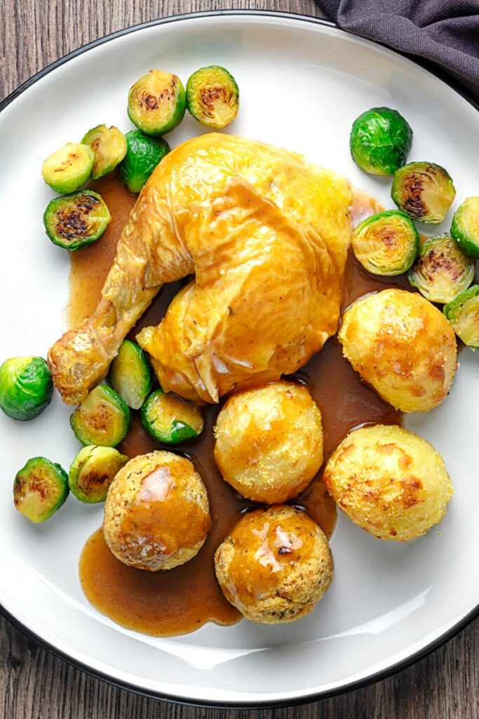 Portrait overhead image of the perfect roast chicken Sunday Lunch featuring a chicken leg, sage and onion stuffing balls, roast potatoes, sprouts and a pan gravy
