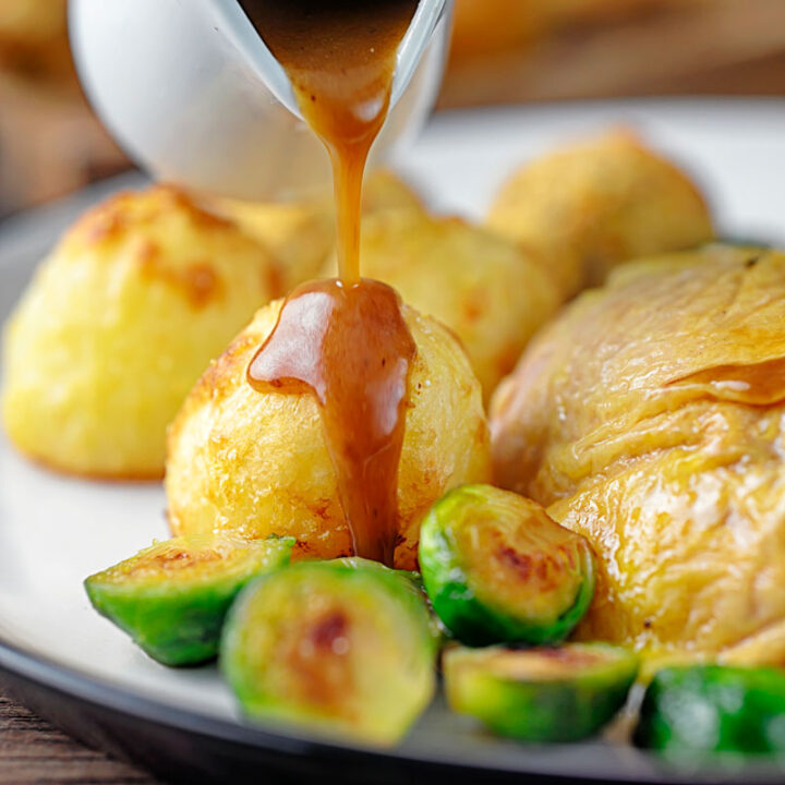 Square image of a perfectly silky gravy being poured over roast potatoes