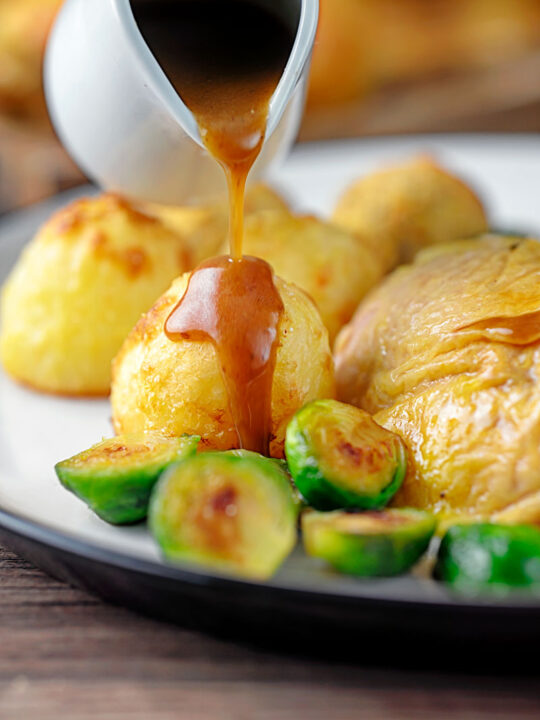 Portrait image of a perfectly silky gravy being poured over roast potatoes