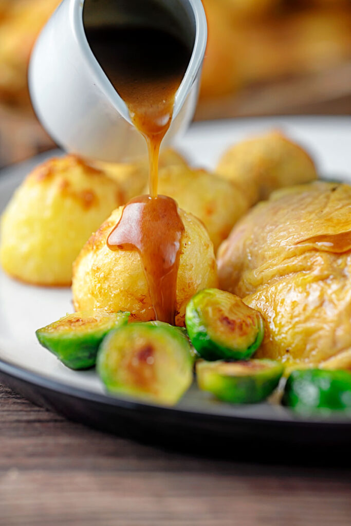 Portrait image of a perfectly silky gravy being poured over roast potatoes