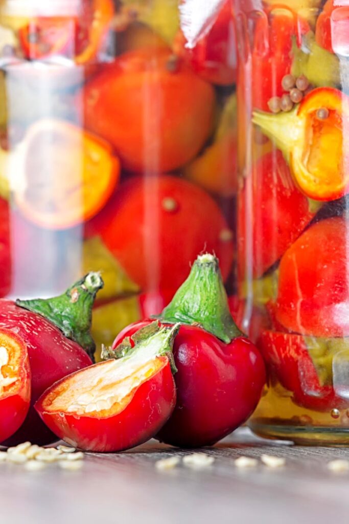 Portrait close up image of cherry bomb chillies in front of jars full of pickled chilli