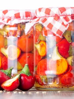 Portrait image of cherry bomb chillies in front of jars full of pickled chilli