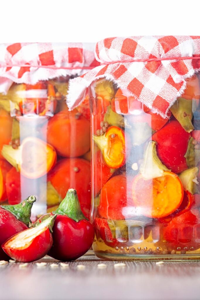 Portrait image of cherry bomb chillies in front of jars full of pickled chilli