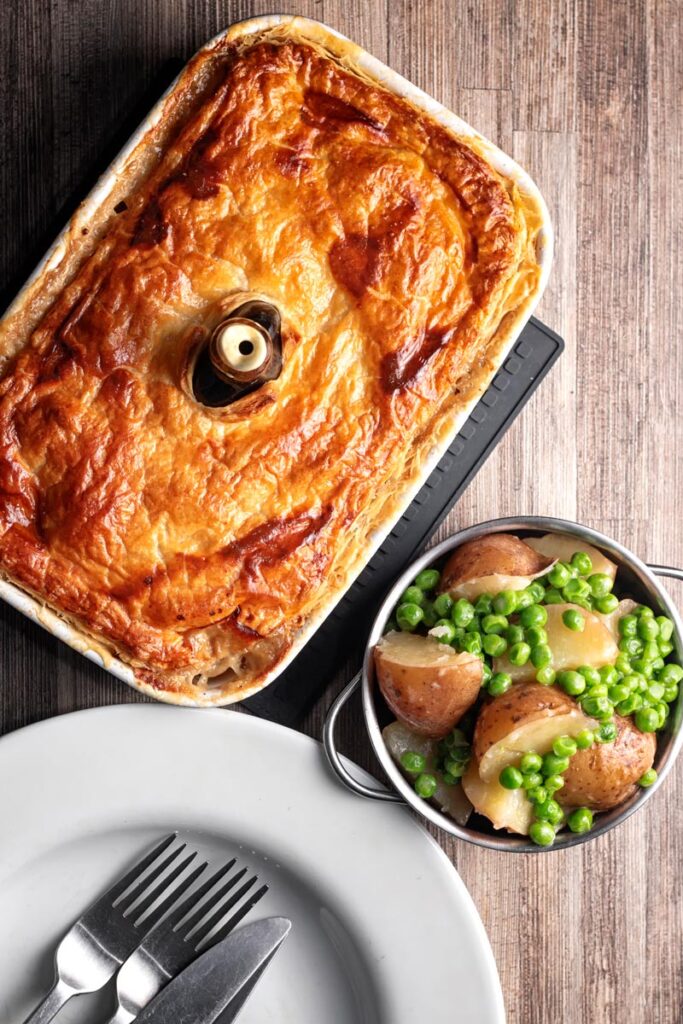 Portrait overhead image of a pork and apple pie with a puff pastry crust served with buttered peas and potatoes