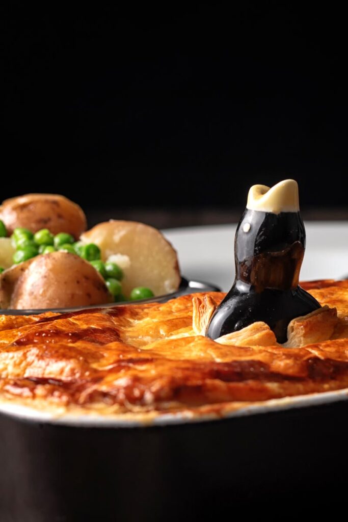 Portrait close up image of a golden puff pastry pie lid with a black bird pie funnel poking through