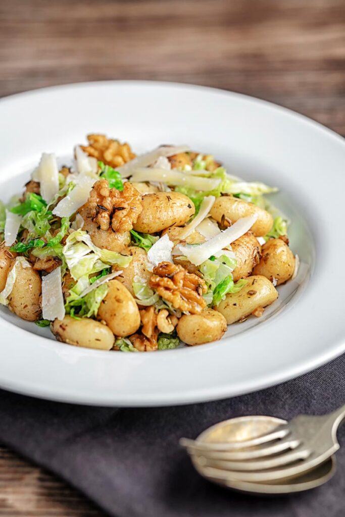 Portrait image of a quick potato gnocchi meal featuring walnuts and cabbage served in a white bowl