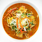 Portrait overhead image of a Thai inspired chicken noodle soup with a garnish of shredded spring onions and red chilli peppers with text overlay