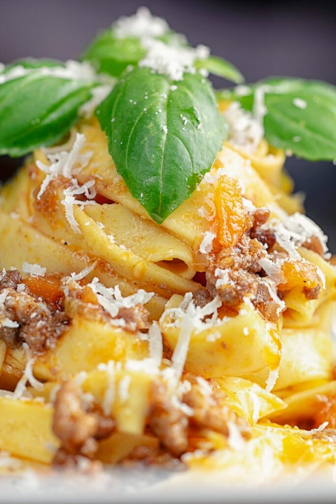 Portrait close up image of pasta served with a ragu bolognese meat sauce served in a white bowl with basil and grated Parmesan cheese