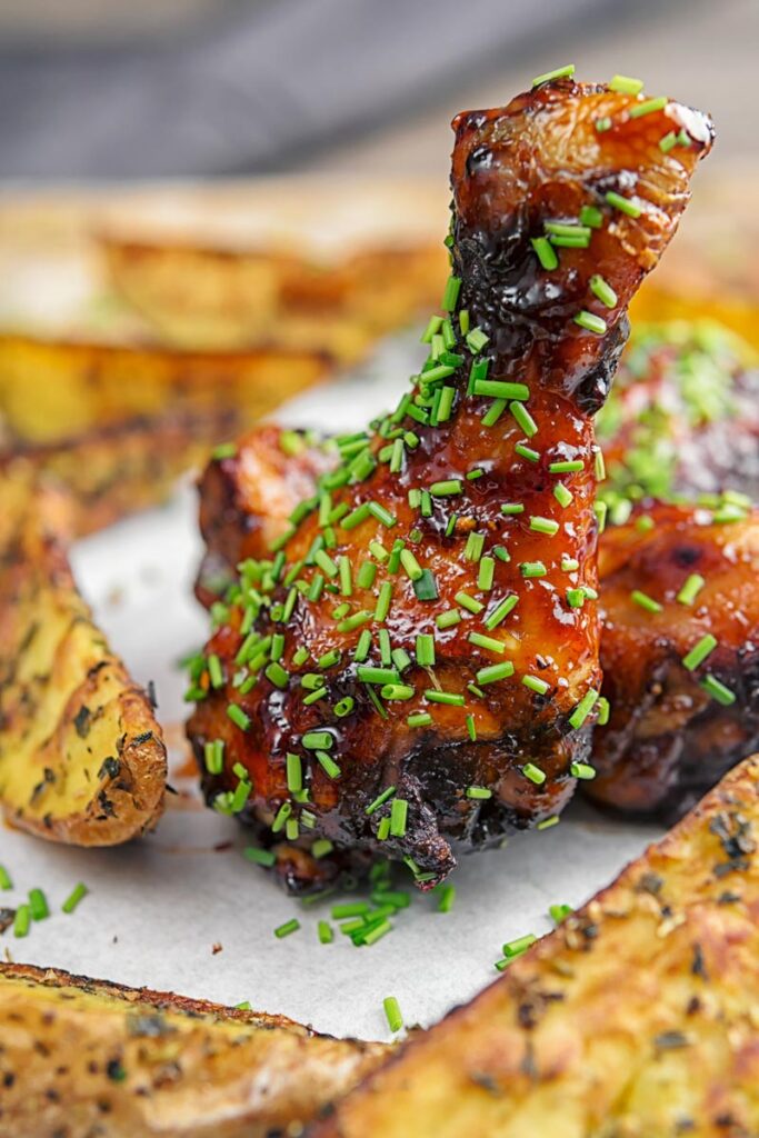 Portrait image of sticky glazed chicken drumsticks with snipped chives served with herbed potato wedges