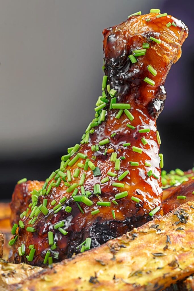 Portrait close up image of sticky glazed chicken drumsticks with snipped chives served with herbed potato wedges