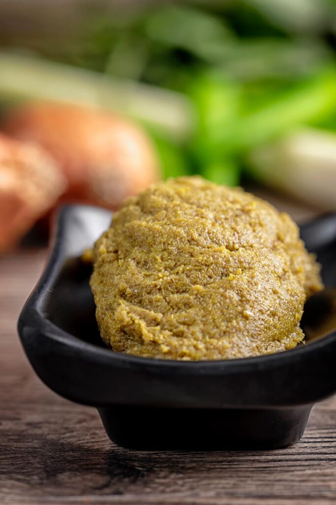 Portrait image of a homemade Thai green curry paste with ingredients for the paste in the background