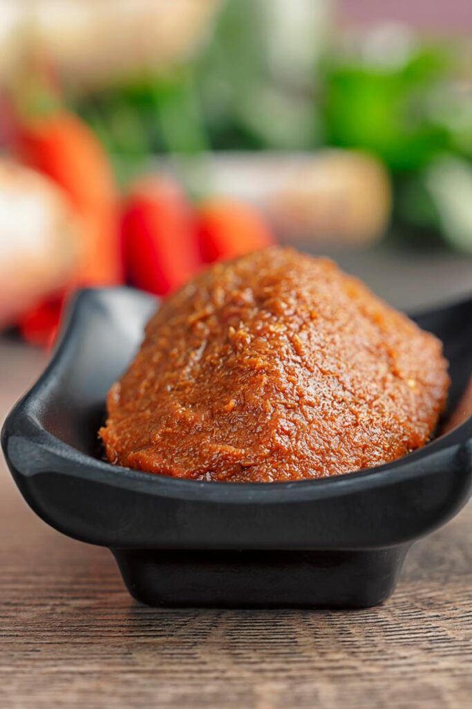 Portrait image of Thai red curry paste on a black serving dish with out of focus ingredients