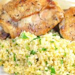 Portrait image of toasted millet served on a white plate with chicken thighs
