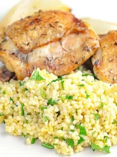 Portrait image of toasted millet served on a white plate with chicken thighs