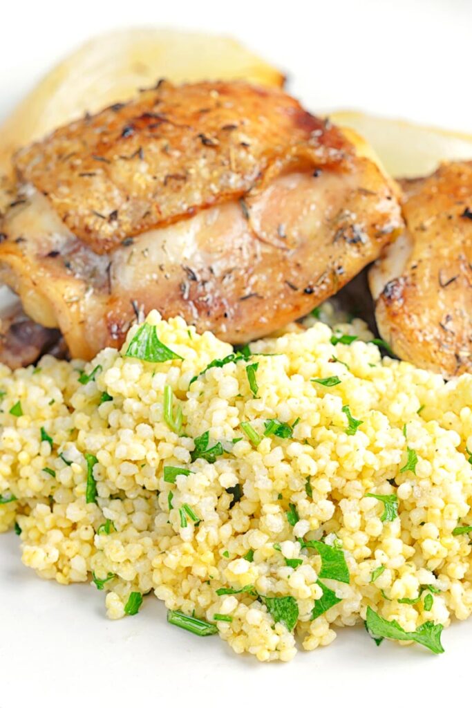 Portrait image of toasted millet served on a white plate with chicken thighs