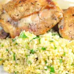 Portrait image of toasted millet served on a white plate with chicken thighs with text