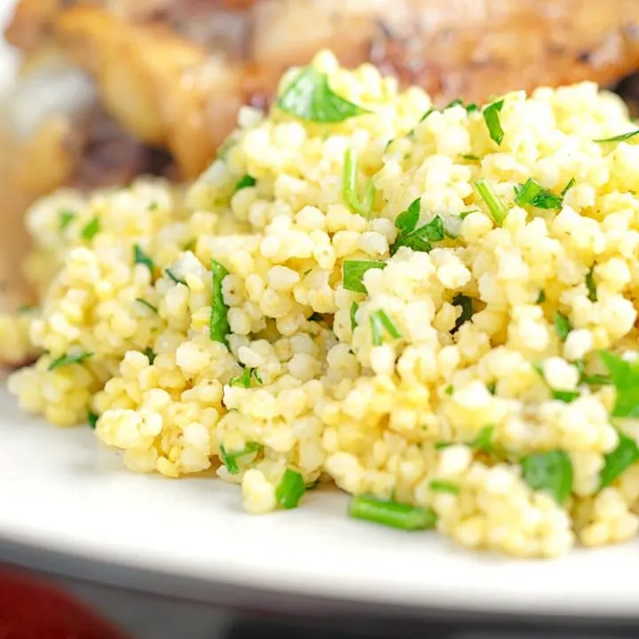 Square close up image of toasted millet served on a white plate with chopped parsley