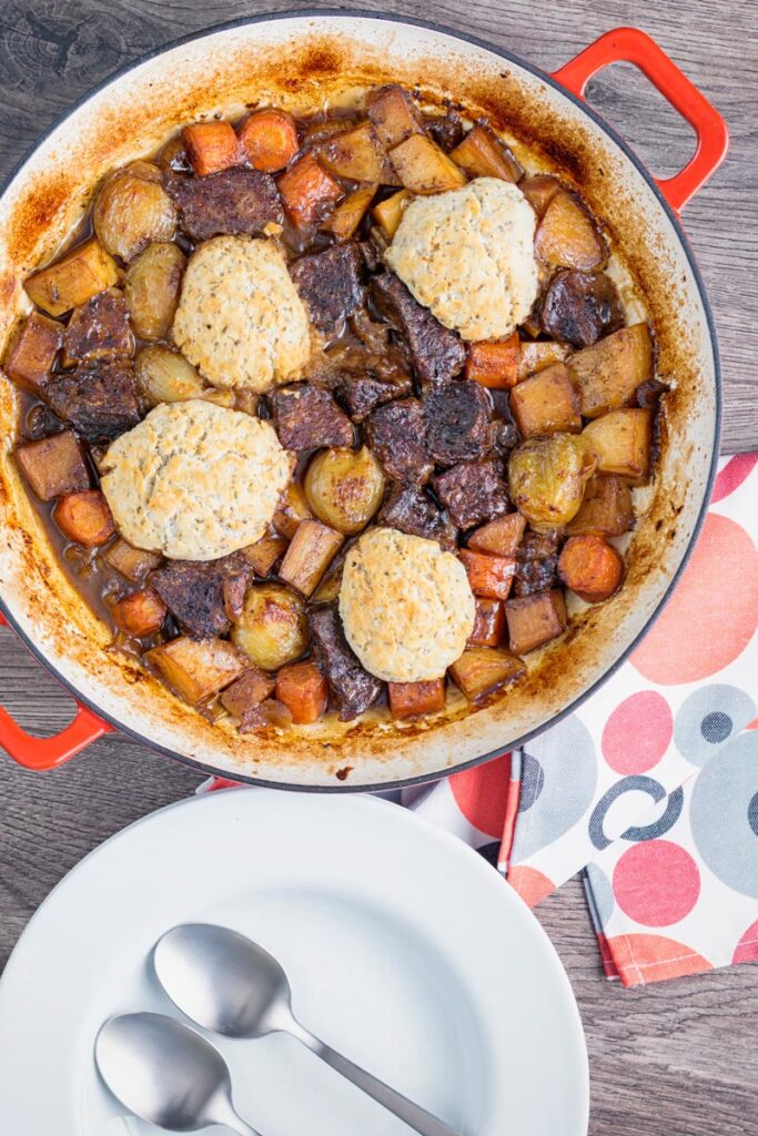Portrait overhead image of a beef stew with suet dumplings and lots of root vegetables cooked in a shallow cast iron pot