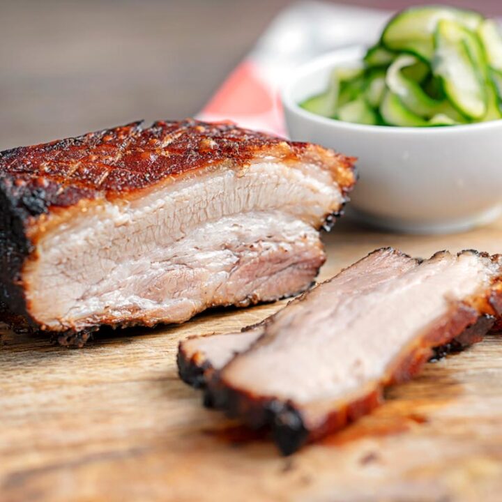 Square image sliced roast Chinese Pork belly with pickled cucumbers on a chopping board