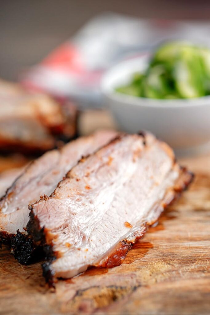 Portrait image of sliced roast Chinese Pork belly with pickled cucumbers on a chopping board