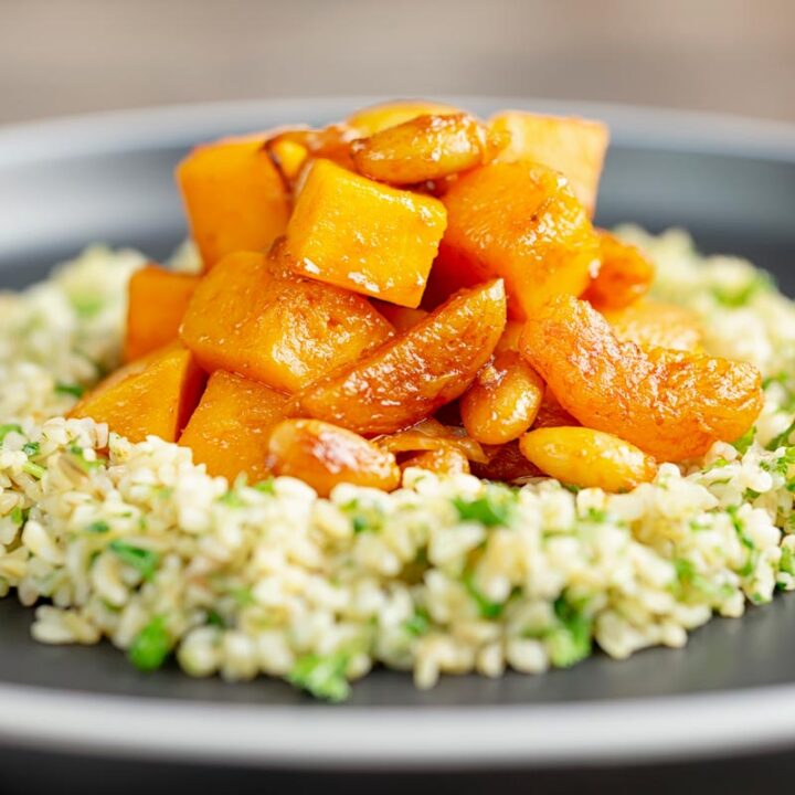 Square image of a butternut squash tagine with dried apricots and almonds served on a bed of herbed bulgur wheat